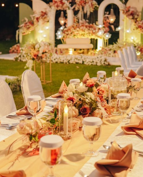 Night dinner long table with white table cloth and an elegant floral arrangement in the middle, set up for a wedding or a special event.